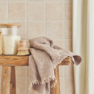En krukke med sitronvask, en skrubb og et beige håndkle på en krakk av tre